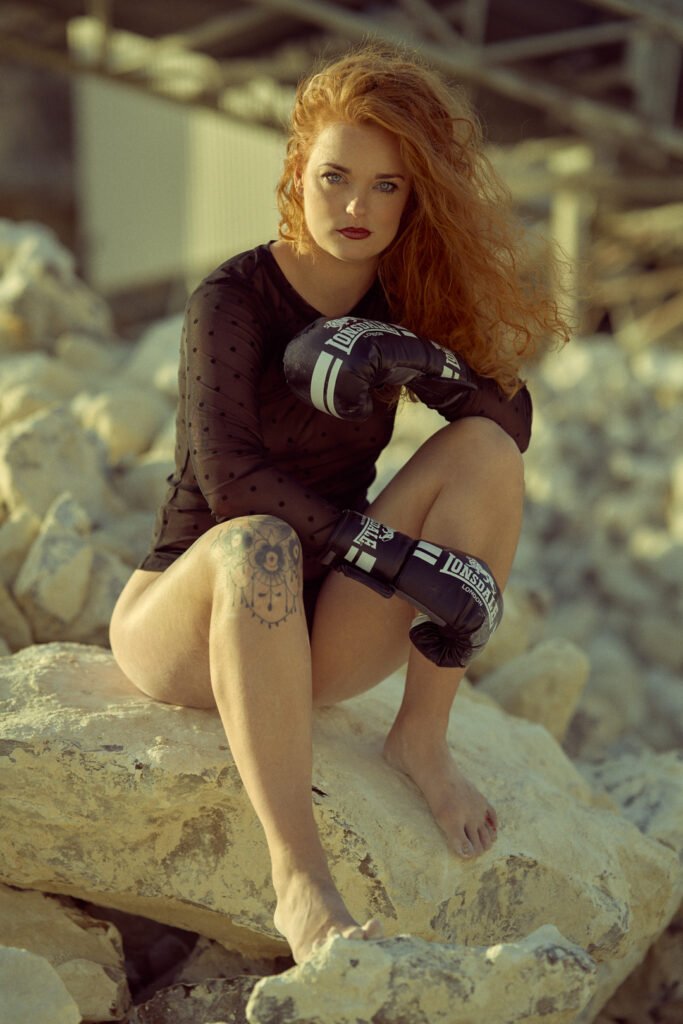A red hair Woman with boxing gloves is sitting on the rock.