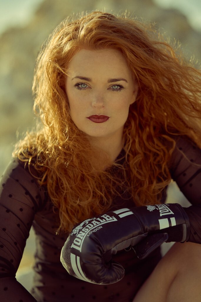 A red hair Woman with boxing gloves is sitting on the rock.